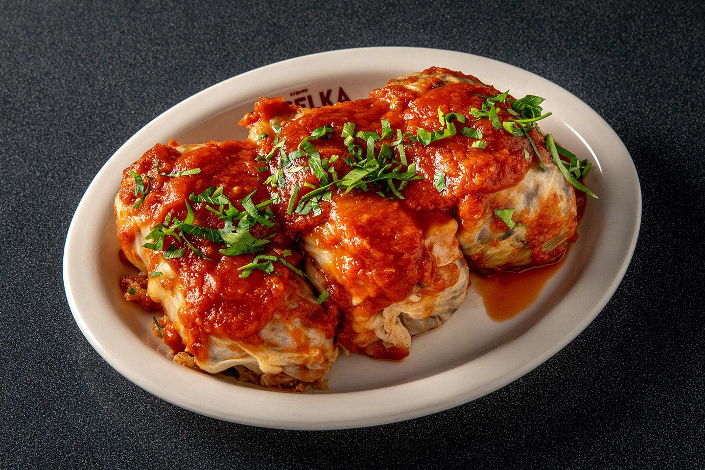 6 Stuffed Cabbage on a serving plate with red sauce a basil on top. 