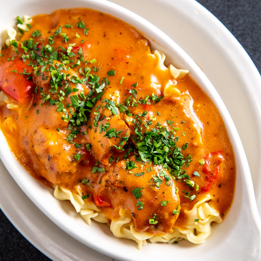 Chicken Paprikash with parsley sprinkled over the top, over egg noodles 