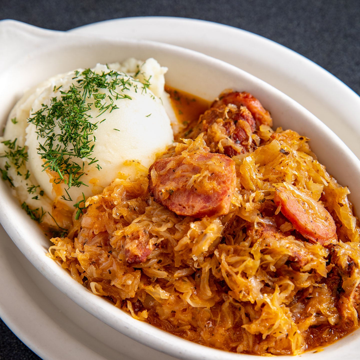 Bigos with mashed potatoes in a white dish, close up