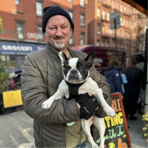 Veselka customer holding his black and white dog showing off that Veselka is dog friendly restaurant, outside with the veselka van in the background