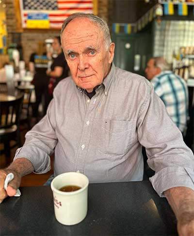 Long time Veselka customer posing in the dining room, older man in a grey shirt with a cup of coffee in front of him