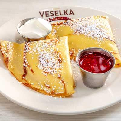 Blintz on a white plate with raspberry sauce and sweetened sour cream on the sauce 