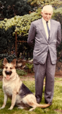 Founder of Veselka with his prized german Shepard, smiling, in a suit, outside and its very green
