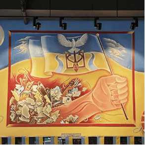 Veselka stand with Ukraine mural, hand holding ukrianian flag, bursting out of a pile of rubbel