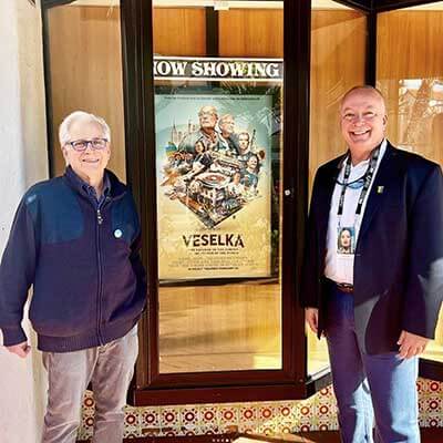 Jason and Tom posing with the Veselka movie poster hung up at a film festival 